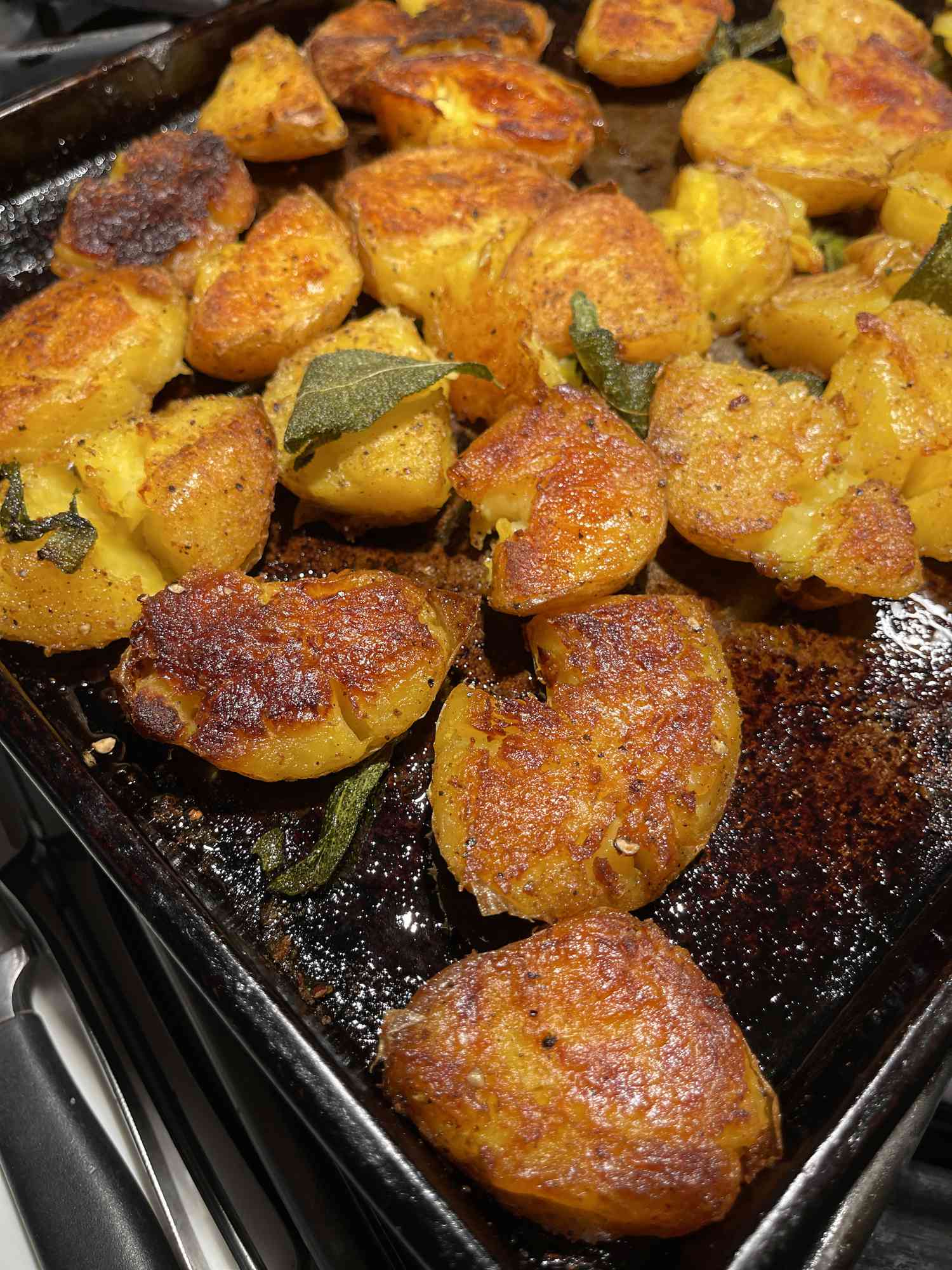 Very brown, crispy potatoes on a baking sheet with sage leaves