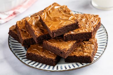 Angle view of a brown and white plate on a marble countertop with a stack of brownies cut into squares