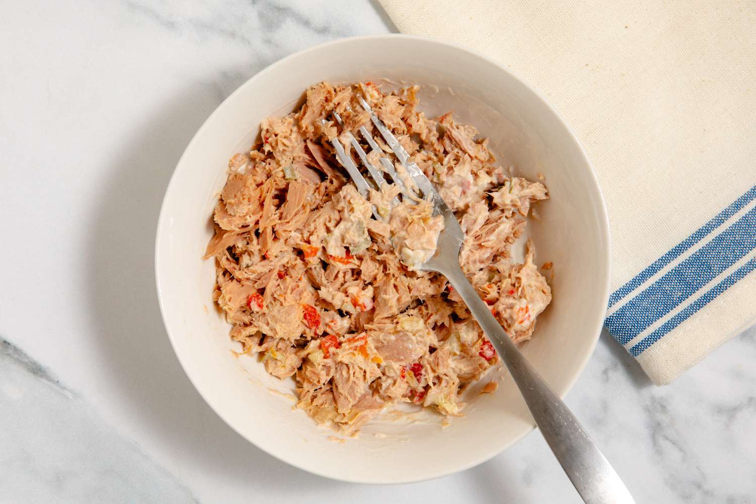 Tuna salad getting mixed together with a fork in a white bowl