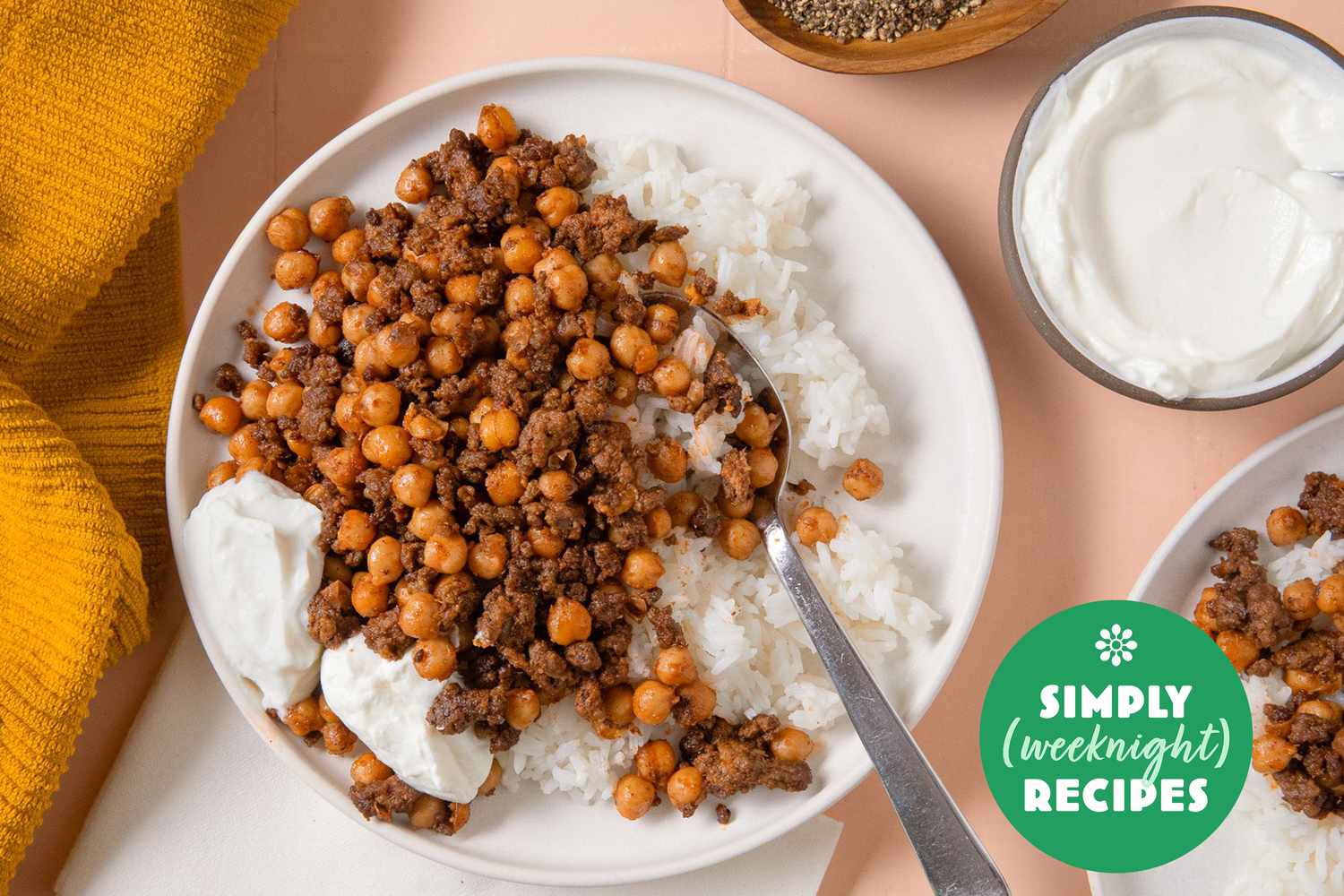 A plate with rice topped with seasoned chickpeas and minced meat, with yogurt on the side, Simply Weeknight Recipes label in view