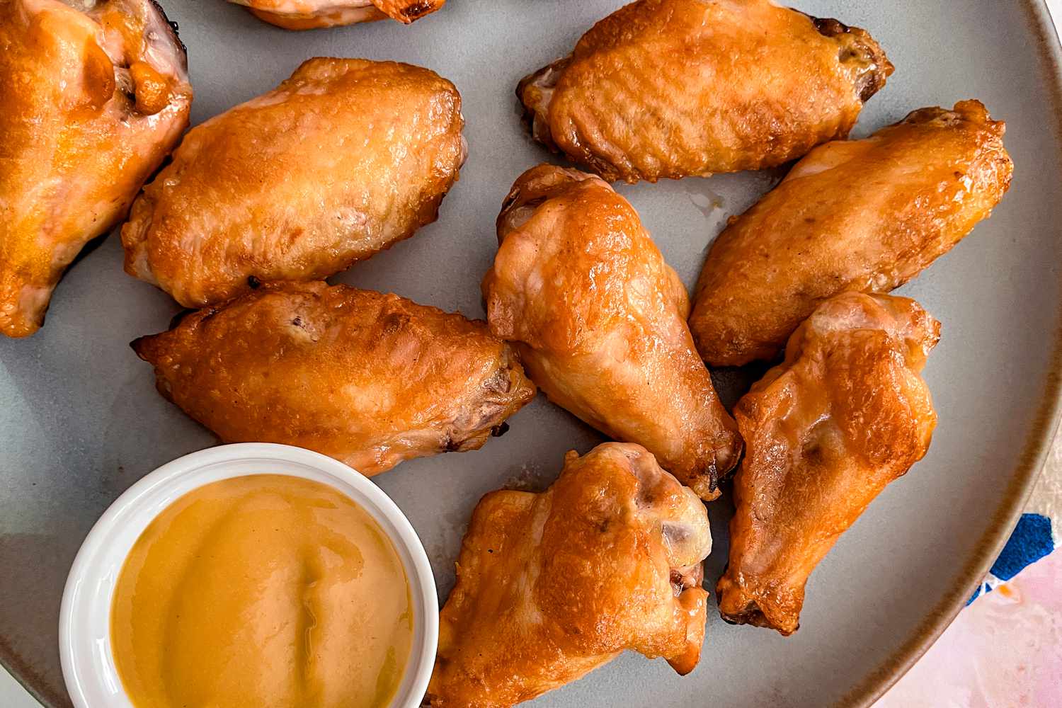 Overhead view of a gray plate of chicken wings with a small bowl of honey mustard for dipping