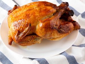 A rotisserie chicken served on a white plate placed on a striped cloth