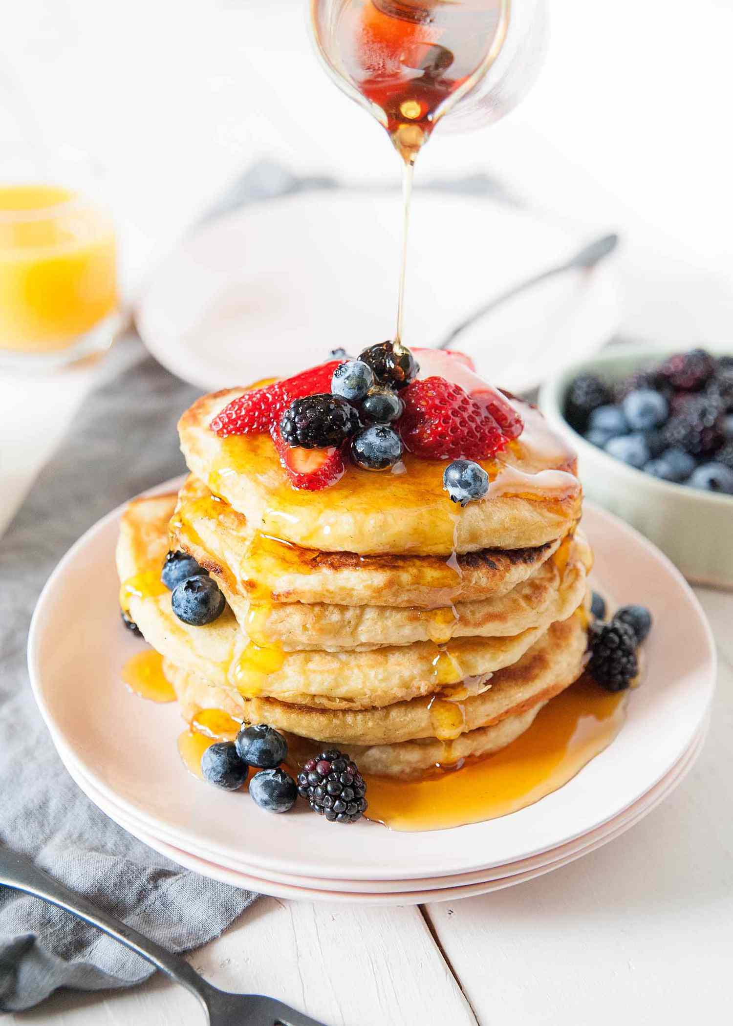 A stack of buttermilk pancakes with syrup raining down on them and berries on top.