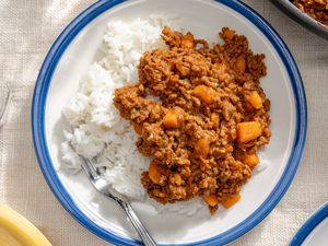 Overhead view of a white plate with a blue rim of picadillo over rice on a white table cloth