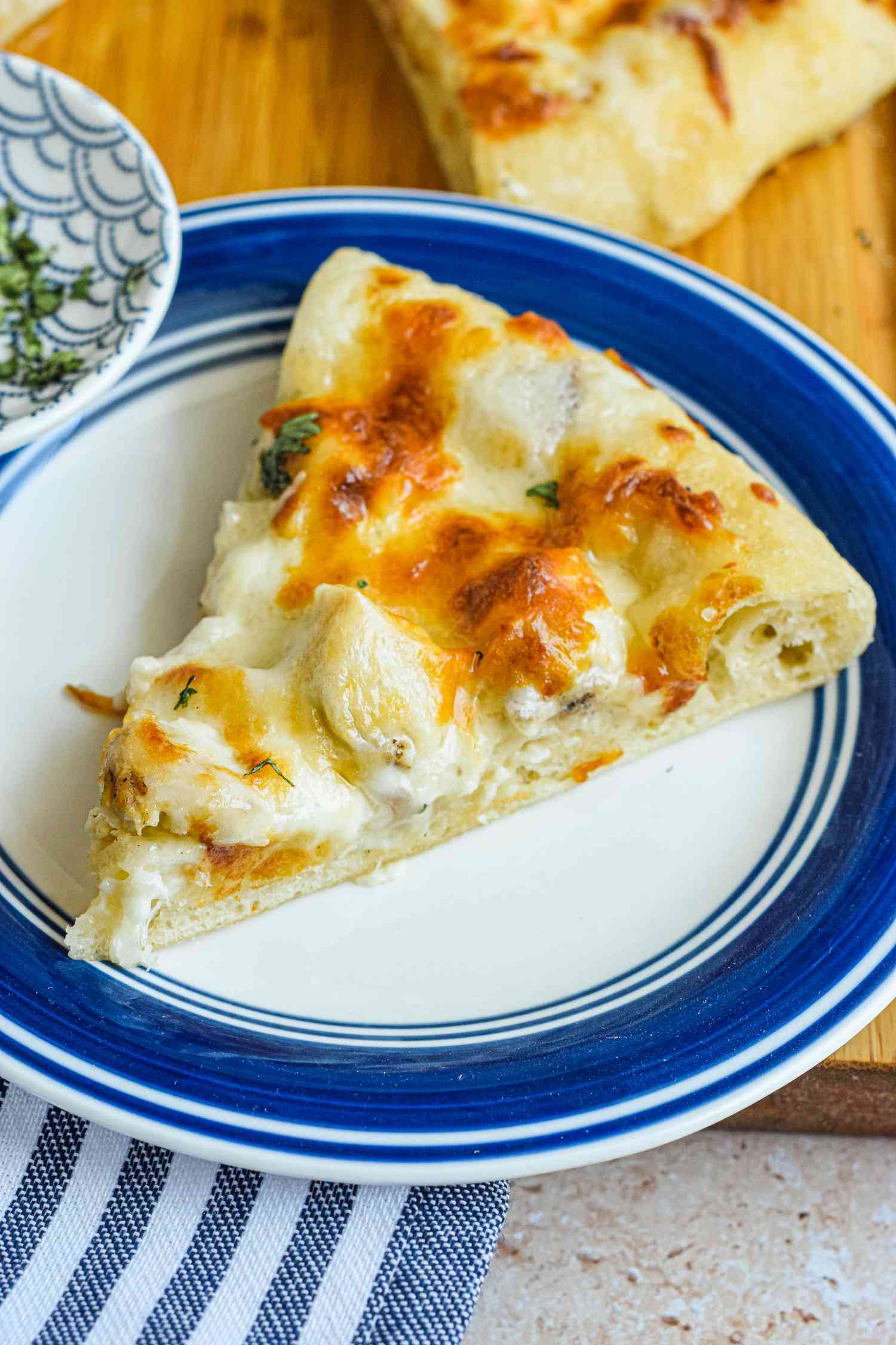Slice of Chicken Alfredo Pizza on a Plate on the Cutting Board, Next to the Rest of the Pizza