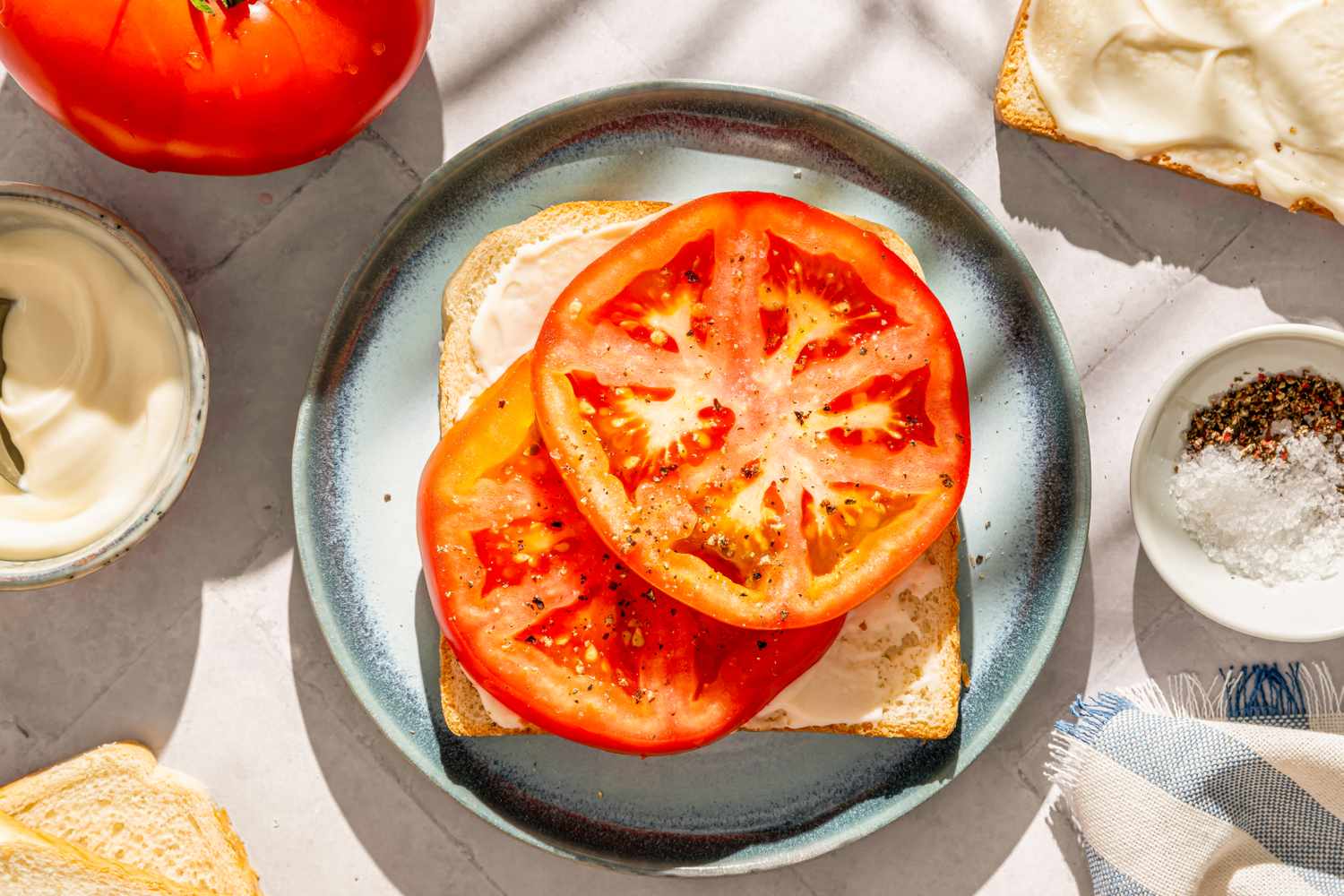 Sandwich with slices of tomato on a plate next to mayonnaise and condiments