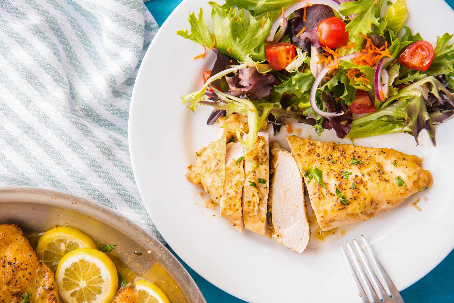Plate of Lemon Pepper Chicken (Half of the Breast Sliced) and Served with a Side Salad, Next to a Pan with More Lemon Chicken and Kitchen Towel