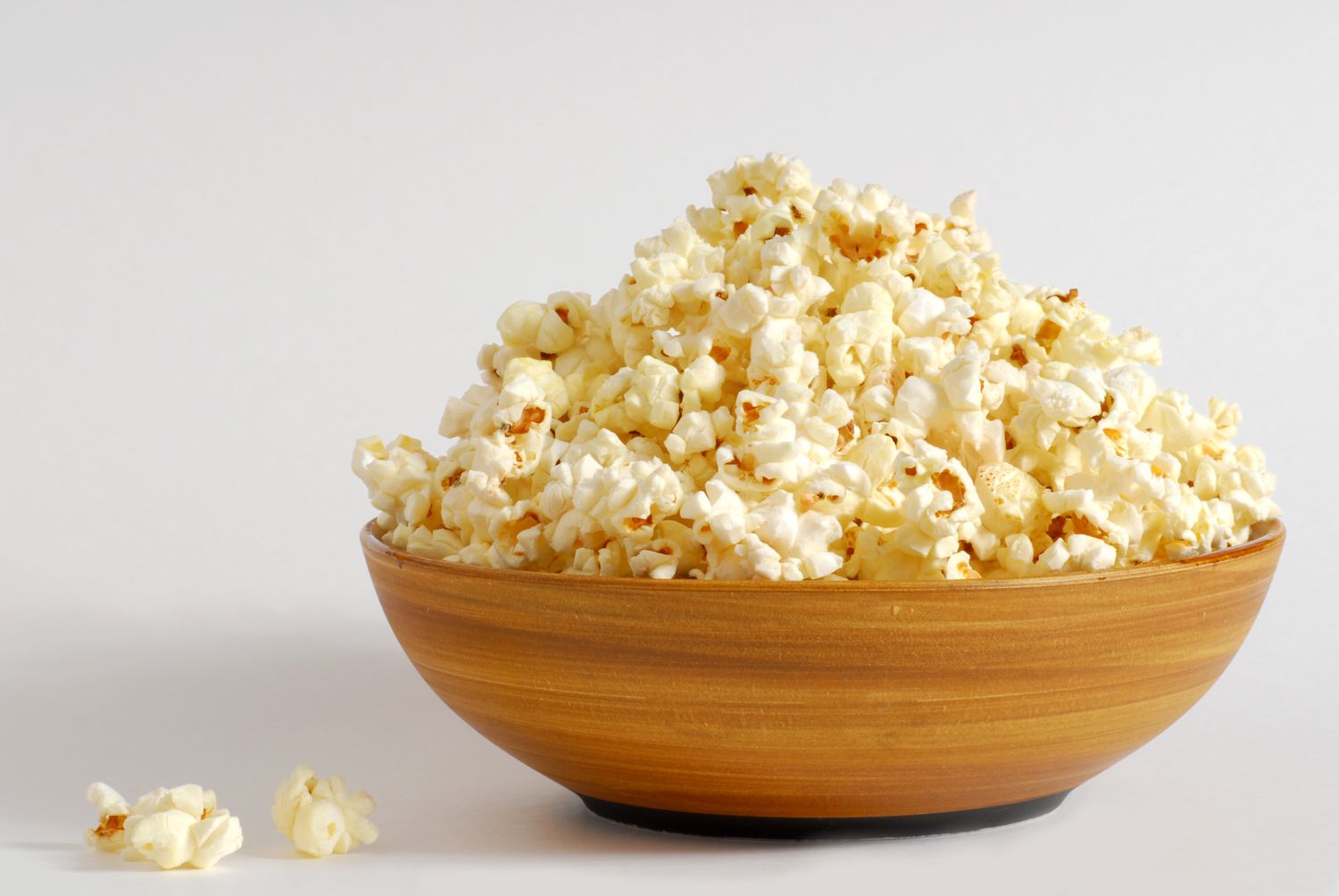 Side view of a large wooden bowl piled high with popcorn on a white background