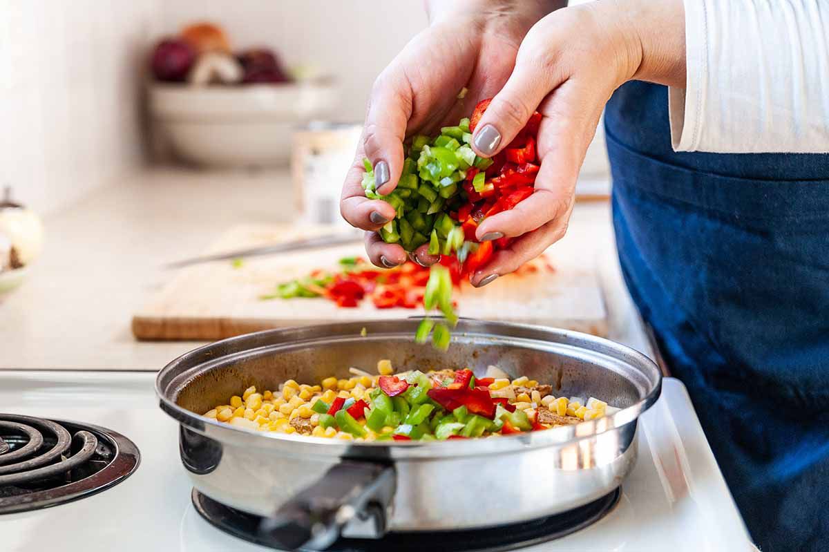 Chicken Recipe in Skillet with Smoked Paprika -- woman's hands adding chopped vegetables to skillet with chicken