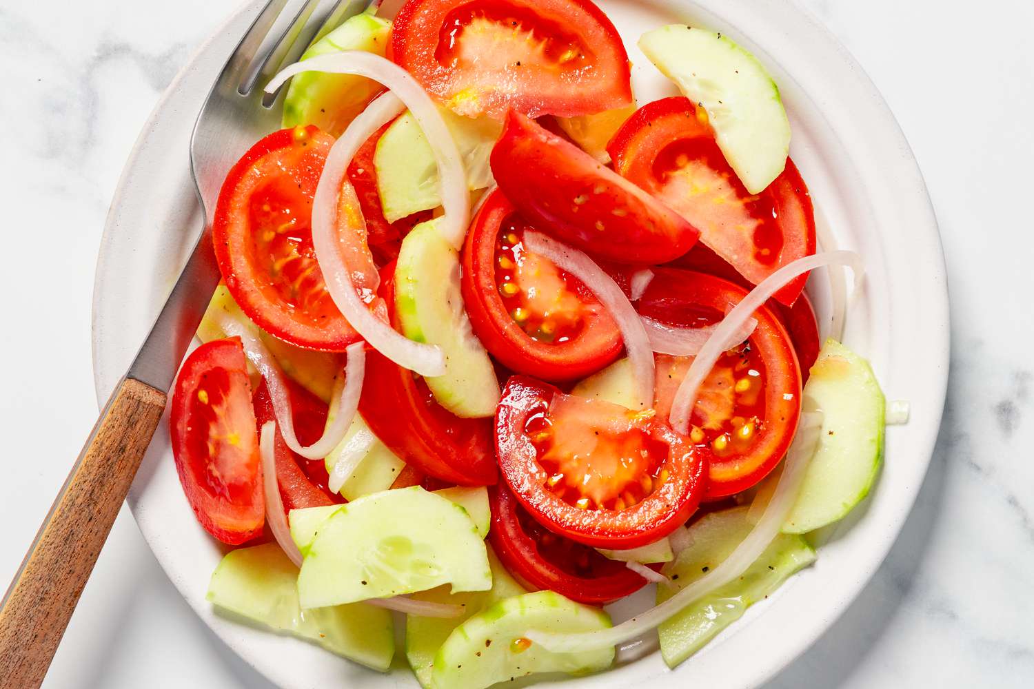 A plate of tomato, cucumber, and onion salad with a fork