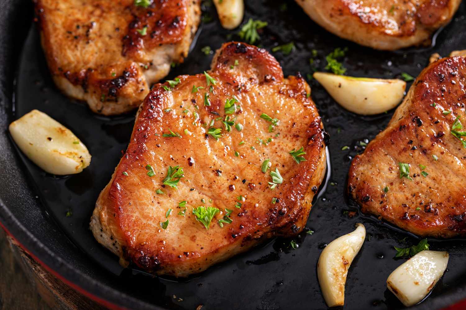 Cooked pork chops in a skillet with garlic cloves and herbs