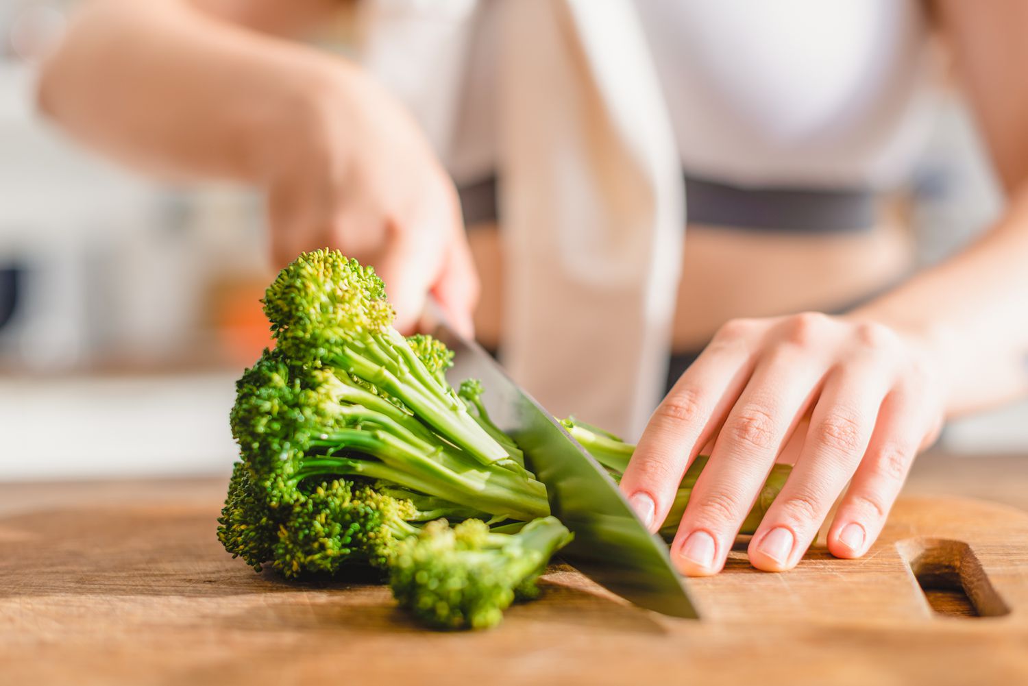 A broccoli getting cut on a wooden cutting board