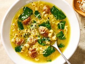Overhead view of a white bowl of Italian wedding soup with spoon and topped with Parmesan cheese