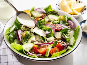 feta dressing spooned onto a salad at a table setting with a bowl of lemon slices, a bowl with feta pieces, a jar with the rest of the dressing, and a table napkin