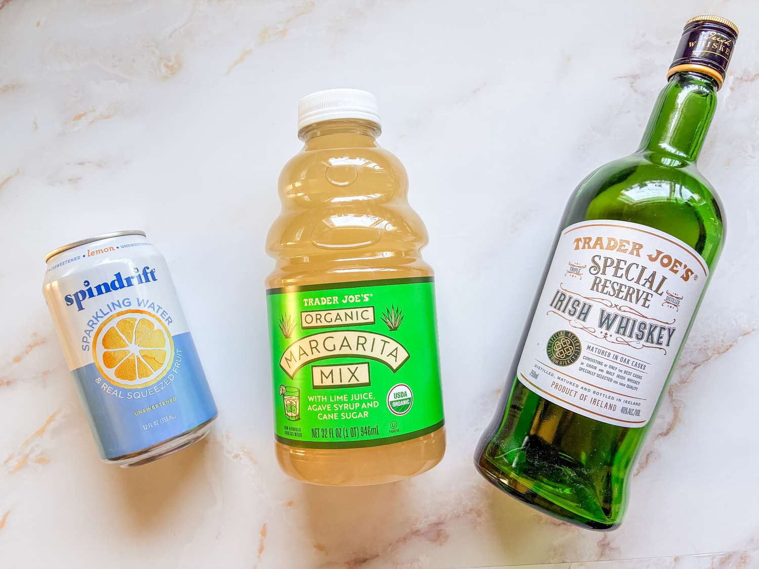 A can of Spindrift sparkling water, a bottle of Trader Joe's organic margarita mix, and a bottle of Trader Joe's Irish whiskey