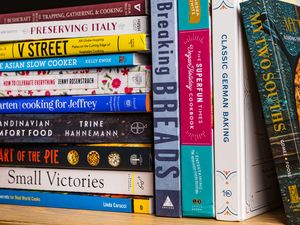 A stack of cookbooks arranged on a shelf showcasing various titles by different authors