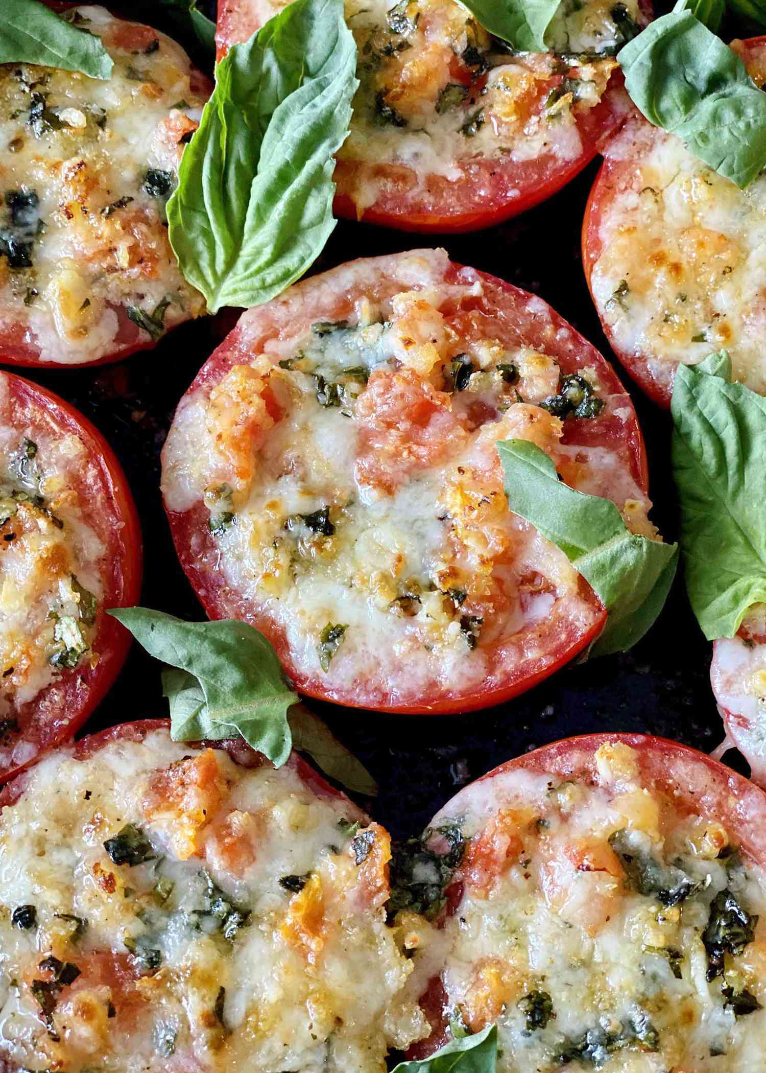 Close up of caprese stuffed tomatoes with basil scattered on top.