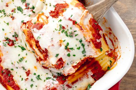 Manicotti Removed From Casserole Dish Filled With Manicotti Using a Wooden Spoon