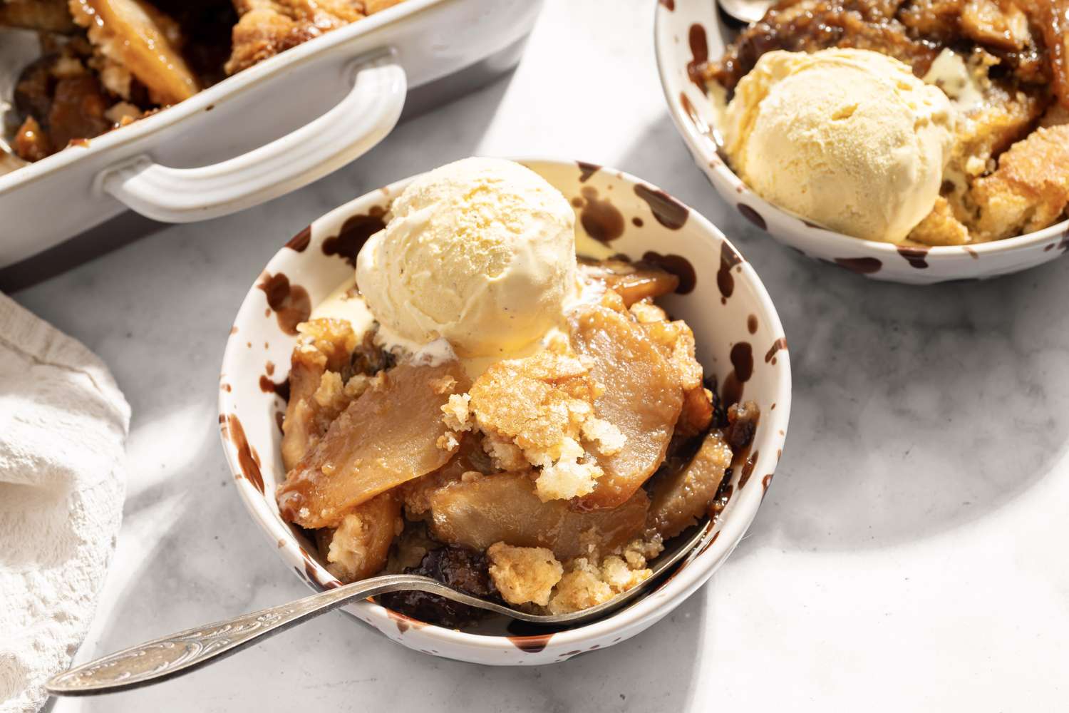 Bowl of caramel apple cobbler topped with ice cream served with a spoon in a dish