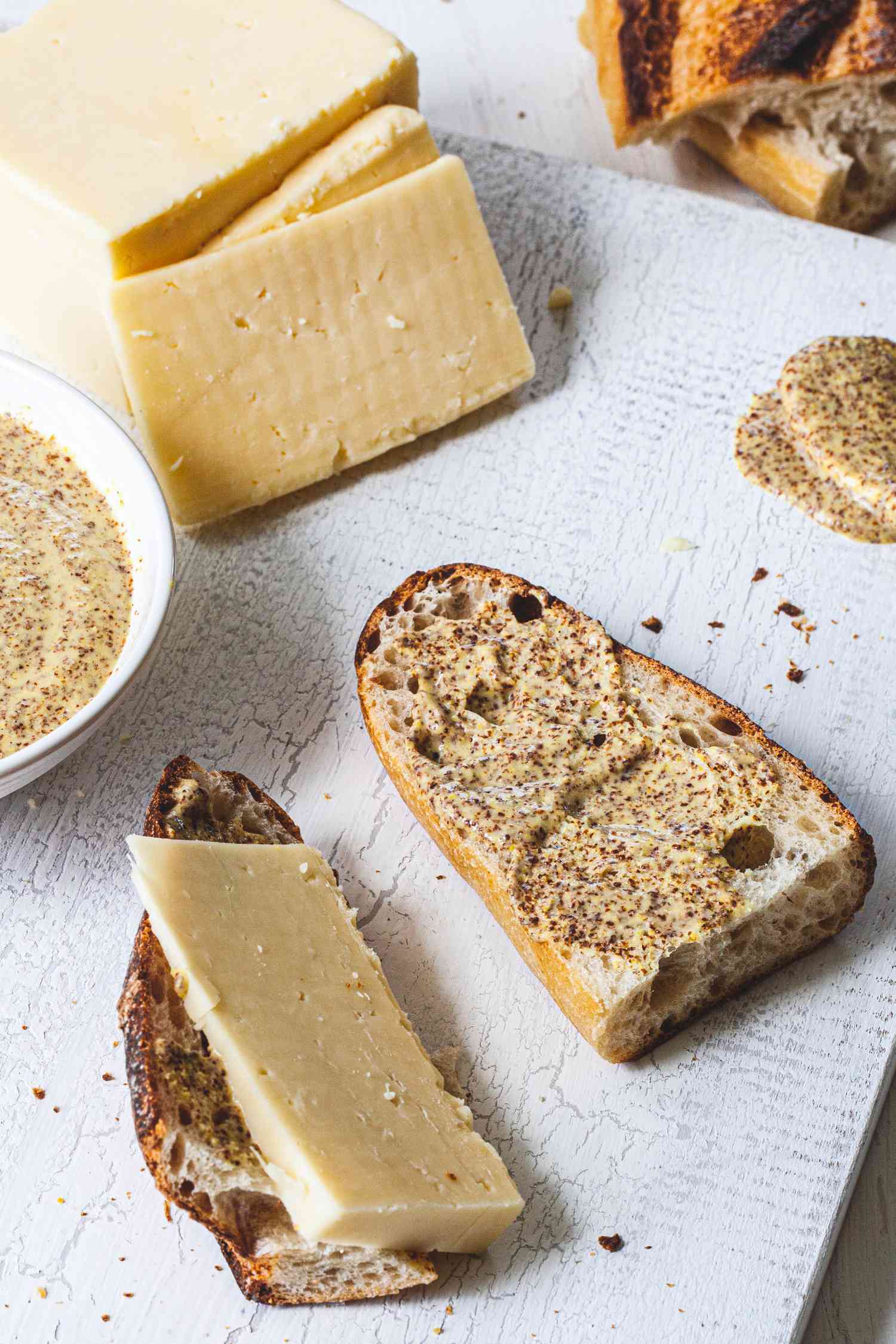Slices of cheese and bread set next to coarse-ground Dijon mustard