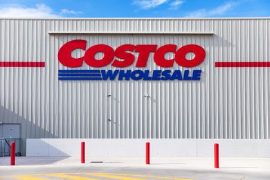 Exterior of a Costco Wholesale store with the logo on the building front four red poles marking the sidewalk