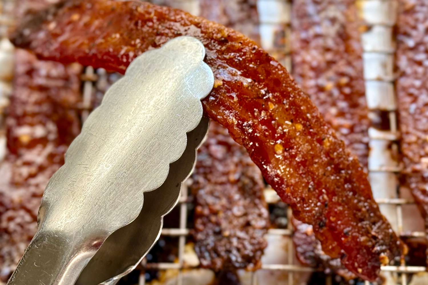Tongs holding a candied bacon strip