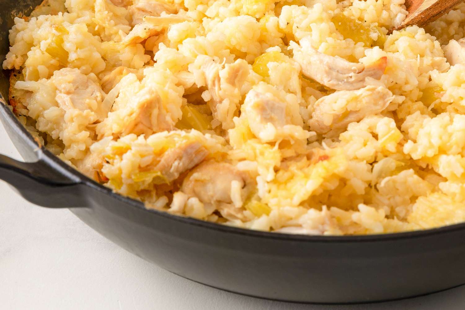 A pan with a dish made of rice and chicken pieces being stirred with a wooden spoon