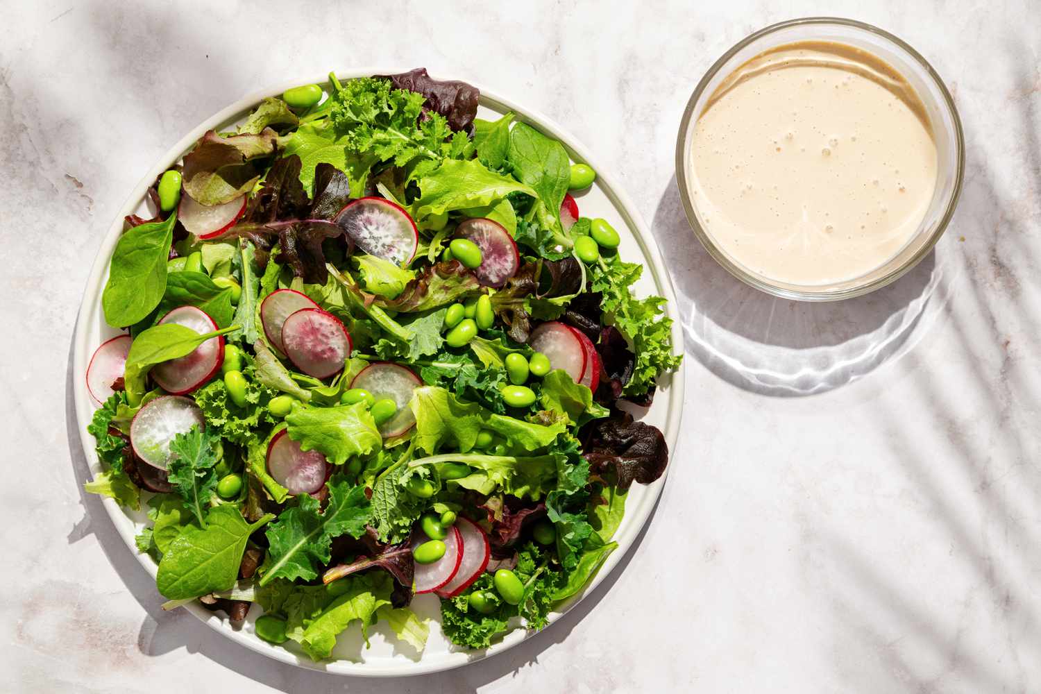 Plate of leafy greens and sliced radishes with a bowl of dressing on the side