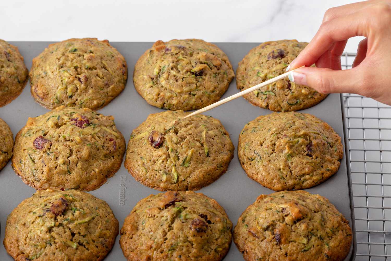 A clean toothpick being held over zucchini muffins showing that they are cooked fully