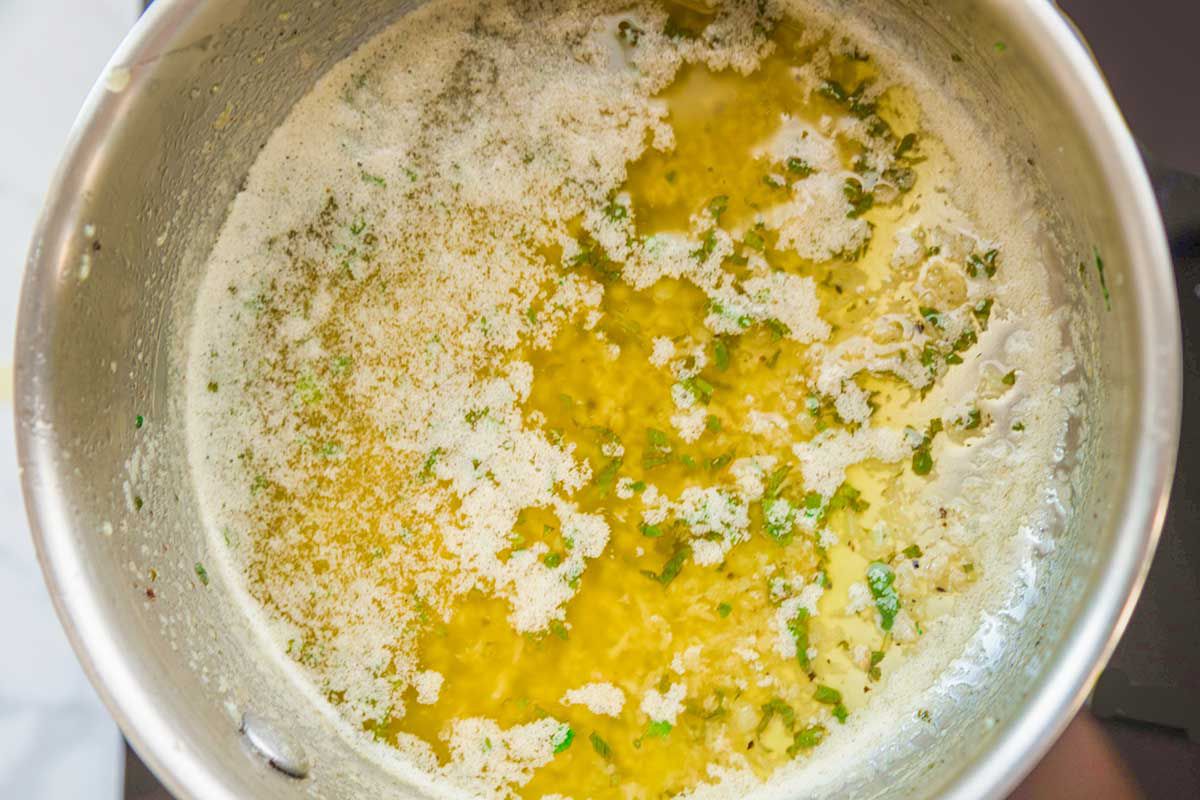 Overhead view of the inside of a metal bowl of al Ajillo sauce. Chopped hervs and melted butter are mixed together in the bowl.