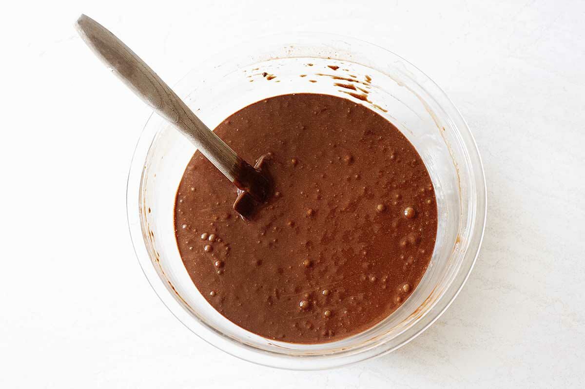 Chocolate cake batter in a glass bowl with a spatula for Authentic Black Forest Cake.