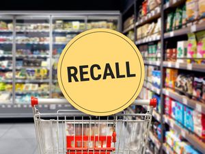 Shopping cart in a grocery store aisle with a large yellow recall sign displayed