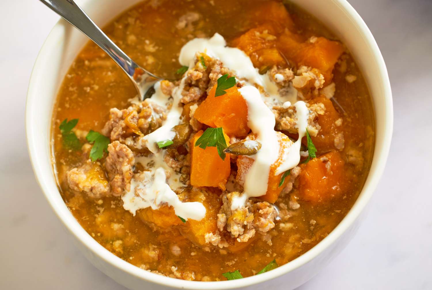 A bowl of butternut squash sausage soup garnished with cream and herbs