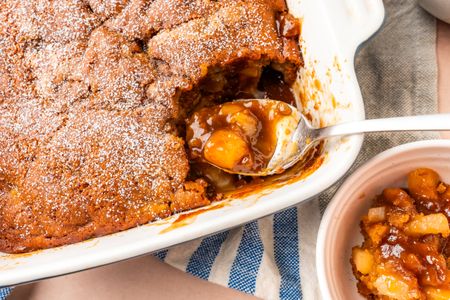 A pear pudding cake in a baking dish with a spoon serving a portion showcasing a dessert with fruit filling
