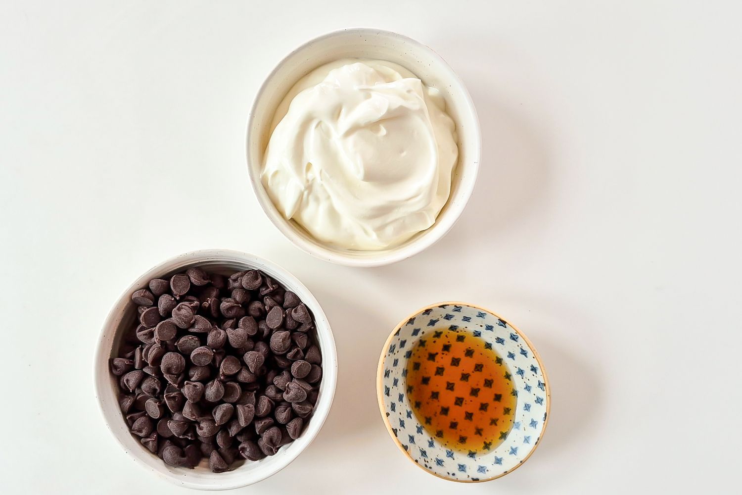 Three bowls containing whipped cream chocolate chips and a liquid