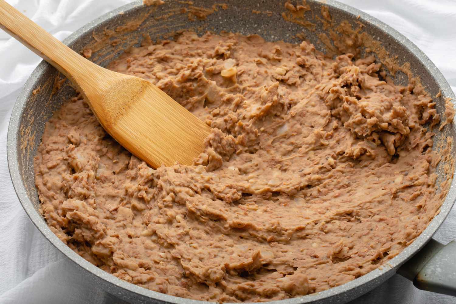 A large bowl of homemade refried beans and a wooden utensil.