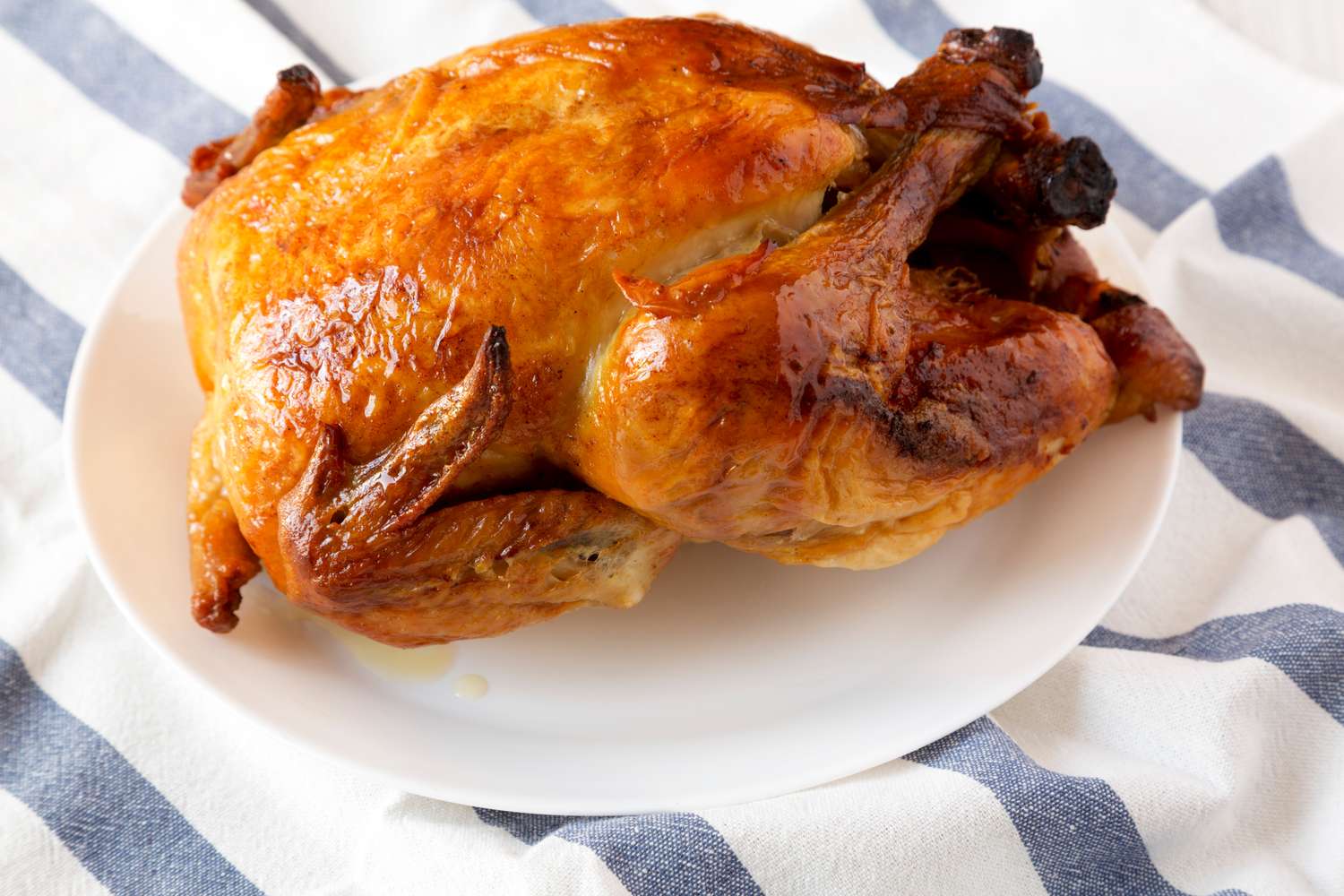 A rotisserie chicken served on a white plate placed on a striped cloth