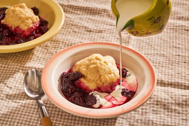 Blackberry slump in a bowl with cream pouring over the top