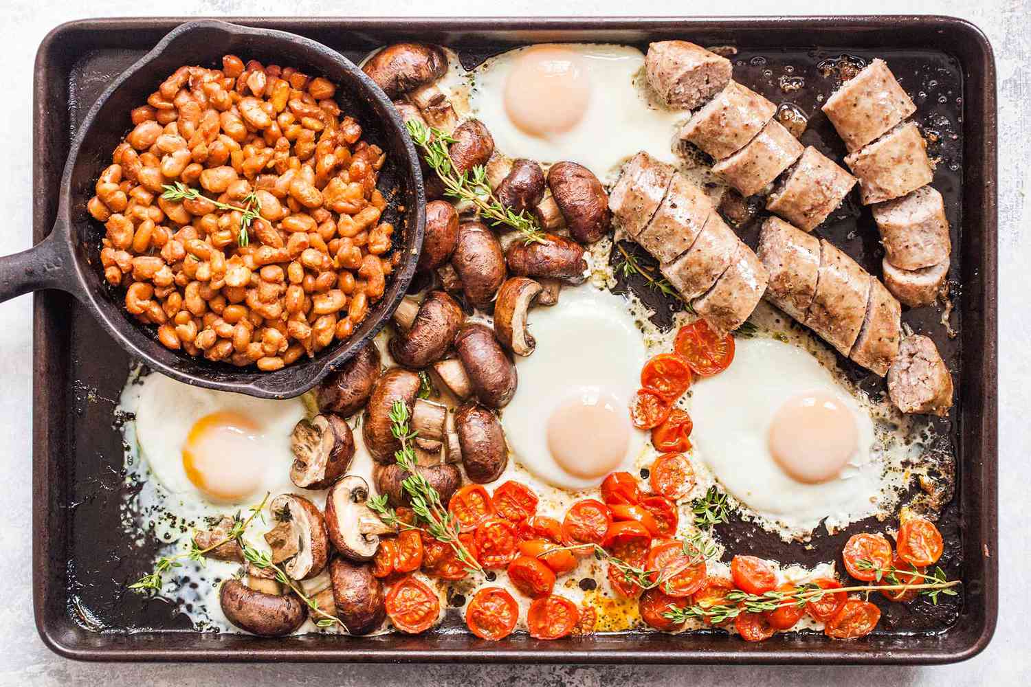 English breakfast on a sheet pan with mushrooms, eggs, beans, tomatoes, and sausage