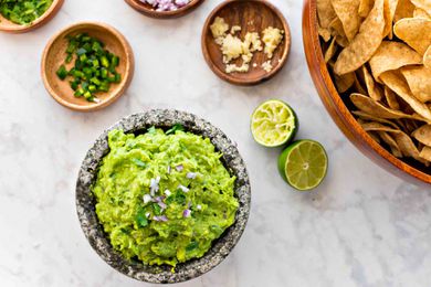 Bright green guacamole in a stone molcajete with a bowl of tortilla chips on the side