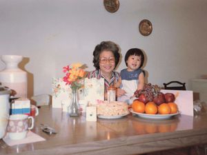 Young Chinese girl sitting at a kitchen table with her grandmother