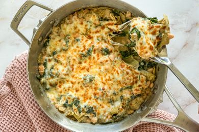 A skillet dish of baked creamy beans with spinach and artichoke topped with melted cheese