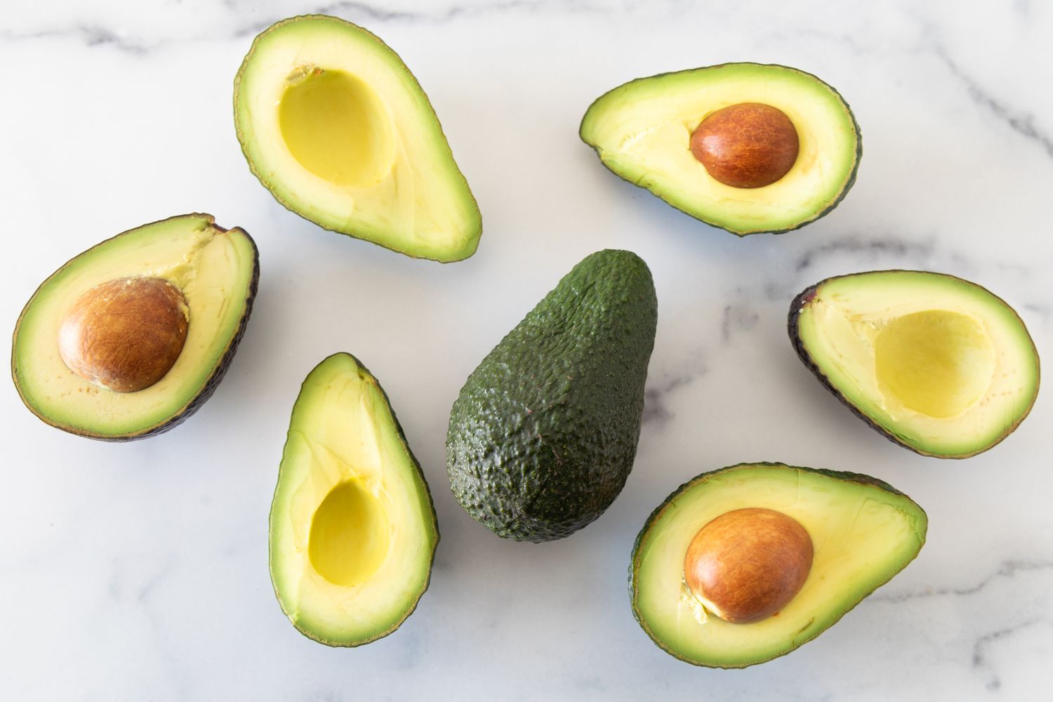 Halved Avocados on a Counter with One Whole Avocado in the Middle 