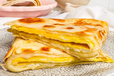Folded egg tortilla on a patterned plate, layered with melted cheese, served with a dish in the background.