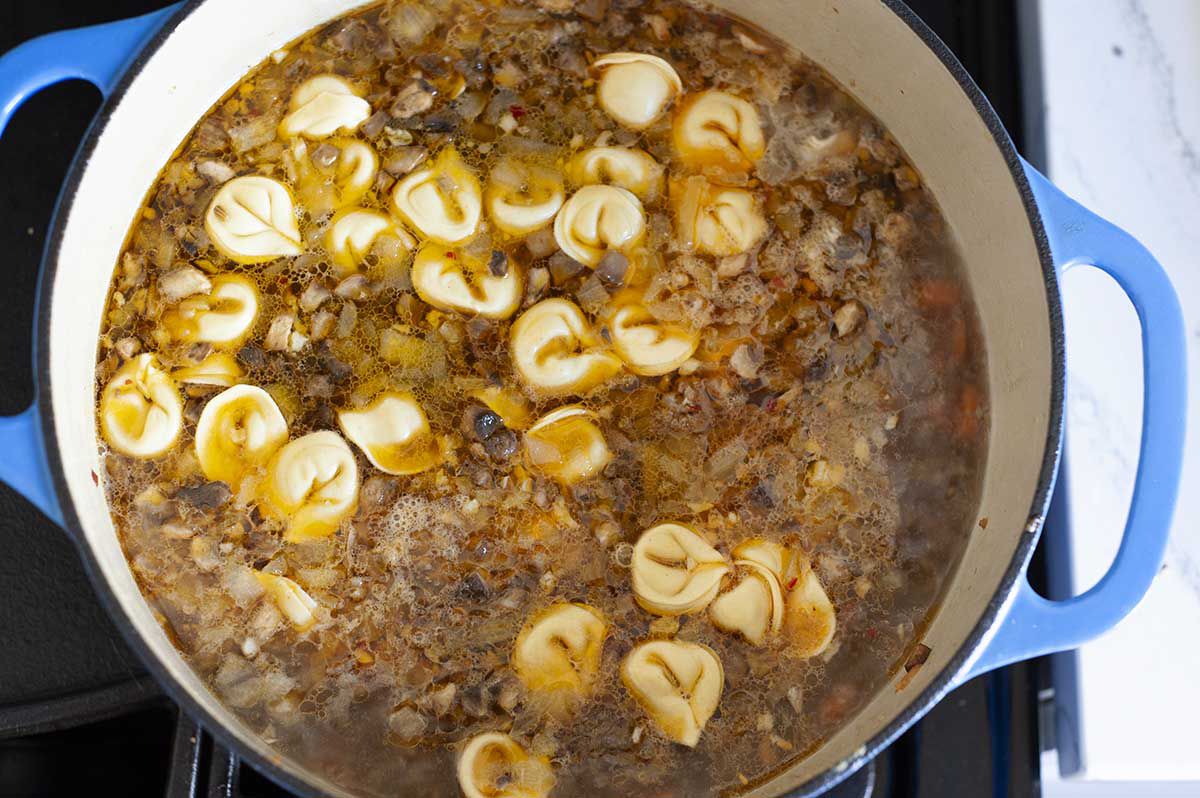 Dutch oven with the best tortellini soup simmering on the stove. Tortellini and broth visible in the pot.