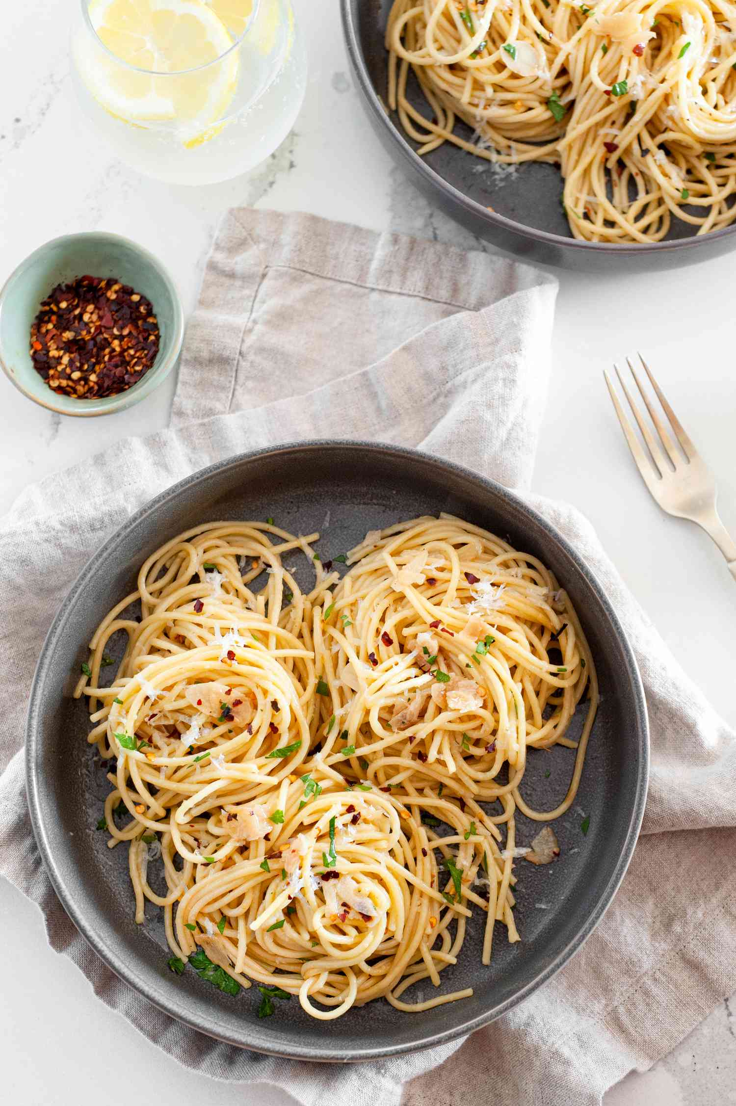 Bowl of Spaghetti Aglio e Olio (Pasta With Garlic and Oil) Topped with Herbs and Parmesan Next to Another Bowl with More Spaghetti