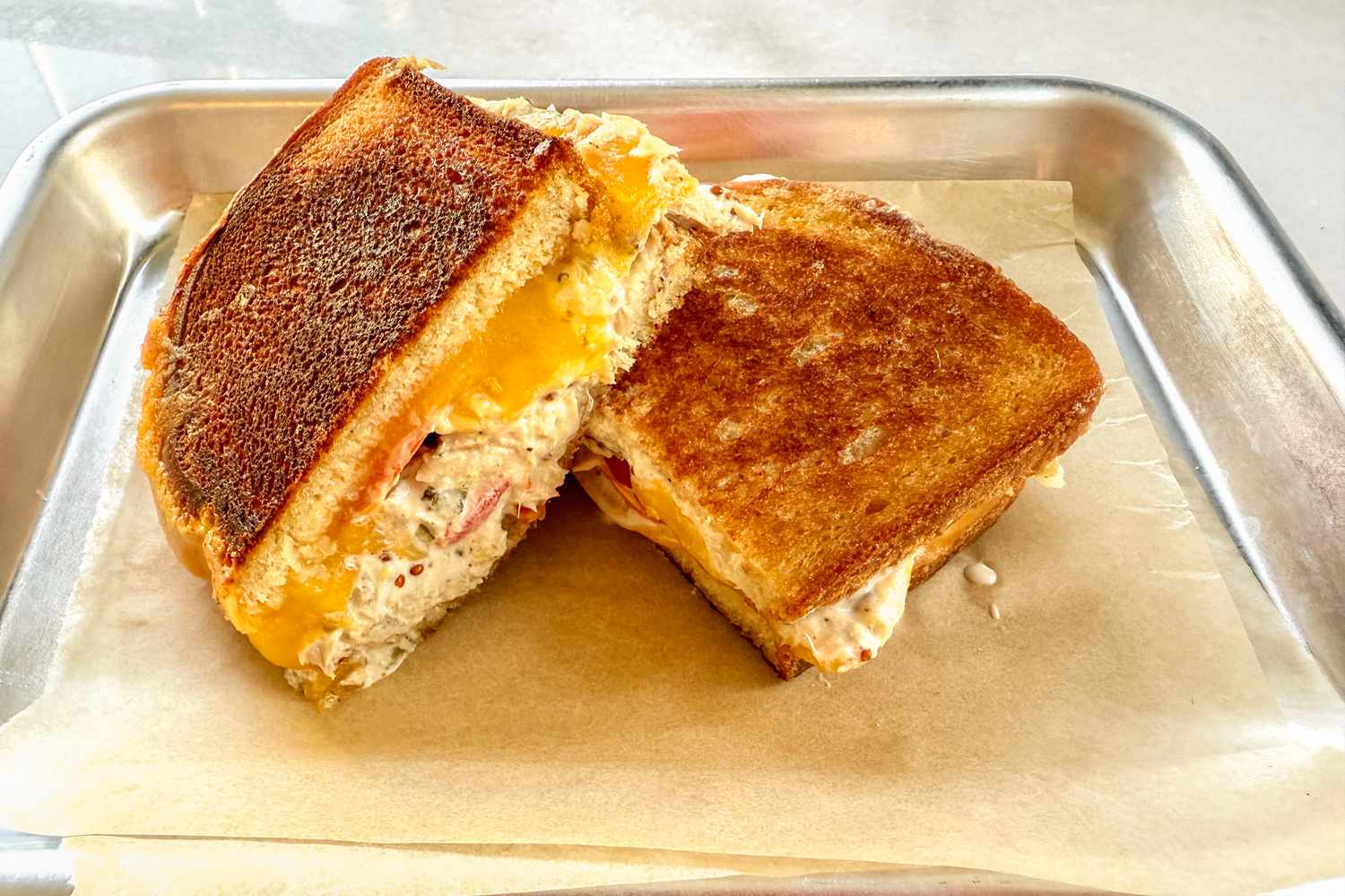 A well-toasted tuna melt cut in half, showing cheddar cheese oozing out the sides
