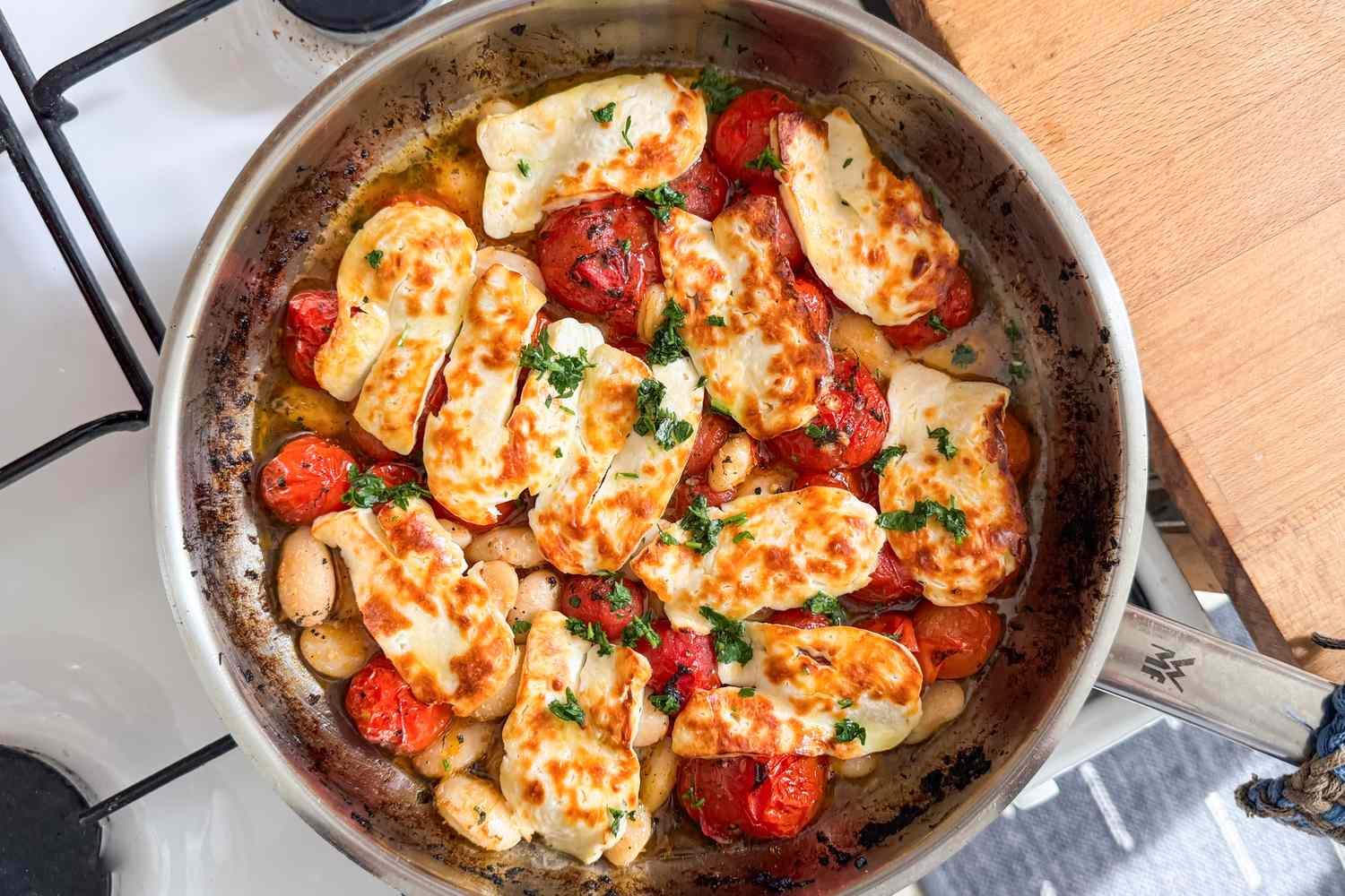 Frying pan with grilled cheese slices cherry tomatoes and white beans topped with parsley for Crispy Halloumi With Tomatoes and White Beans