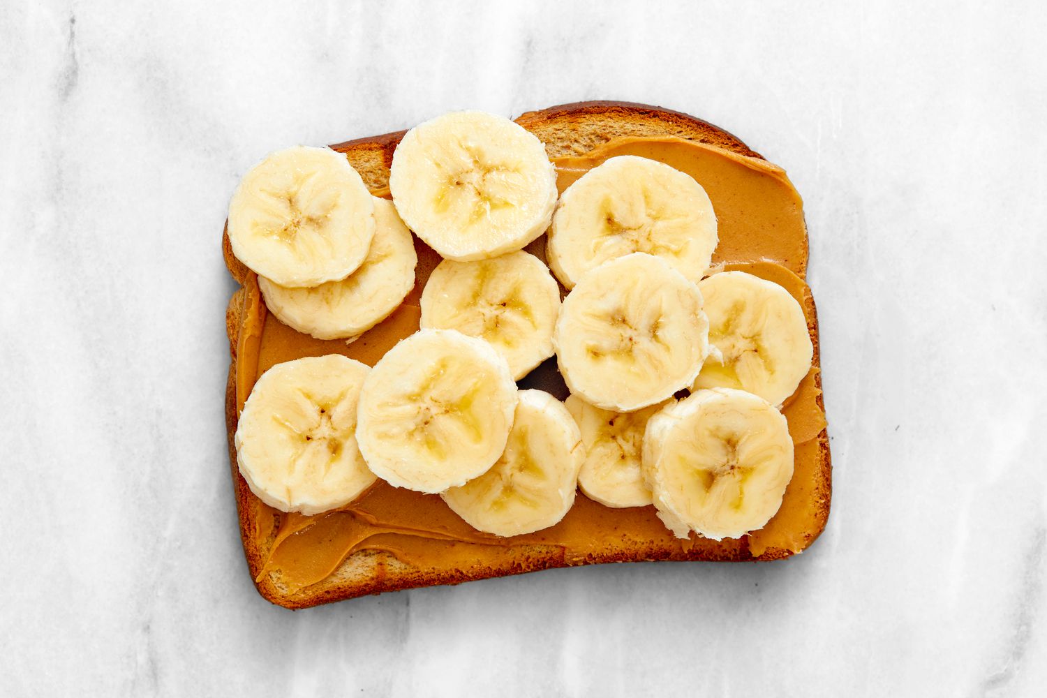 A piece of toast topped with peanut butter and sliced banana on a marble surface