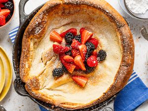 A Dutch Baby pancake topped with fresh strawberries, blackberries, and powdered sugar displayed in a skillet